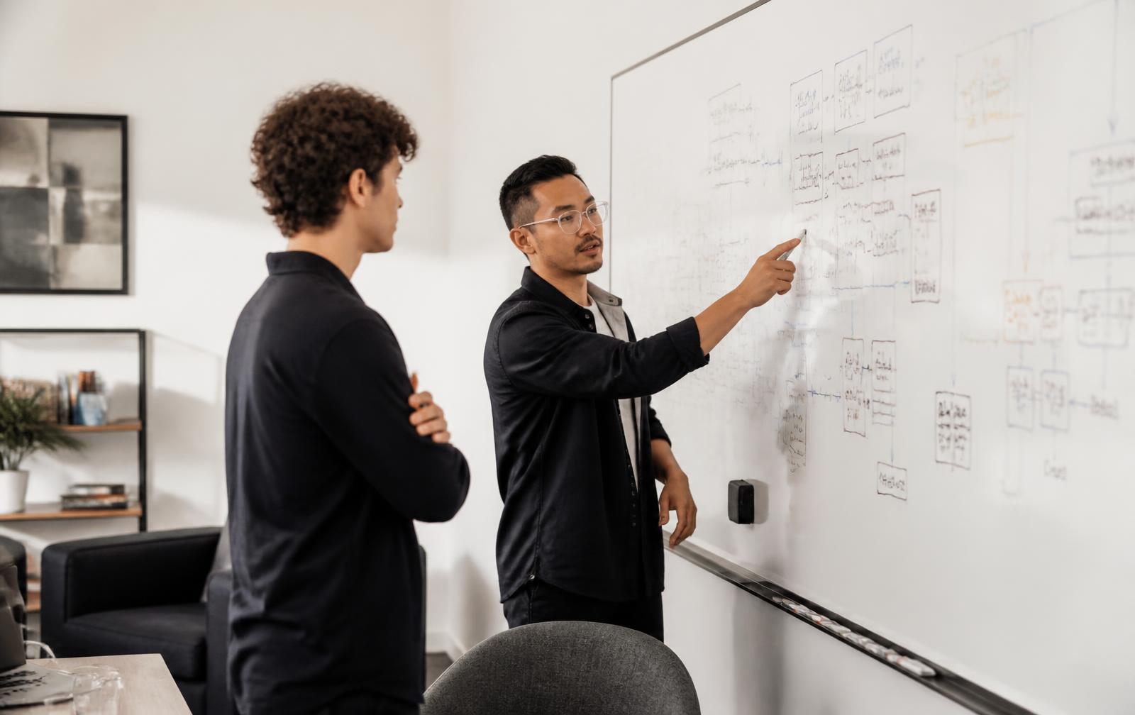 Two colleagues reviewing a hand-drawn software architecture diagram on a whiteboard